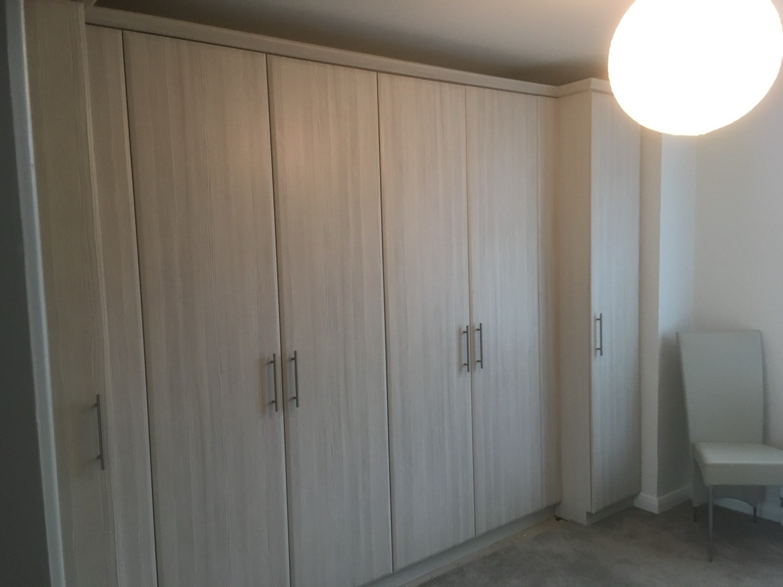 Fitted oak wardrobes with hinged doors running the length of a bedroom wall